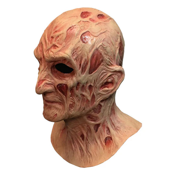 A Nightmare on Elm Street Dream Master Freddy Krueger Deluxe Costume Mask Features a latex full‑coverage sculpt with heavily burned, blistered skin textures, deep scar grooves, and warped facial contours, finished in mottled flesh tones with dark red shading to emphasize rot and damage and distortion that reflects Freddy’s supernatural decay, left profile