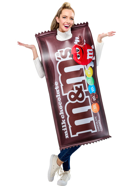 Woman posing in the Adults Milk Chocolate M&M's Costume Featuring a foam-backed tunic costume designed to resemble a milk chocolate M&M’s candy package, with a rich brown wrapper print, large white m&m’s branding across the front, printed colorful candy pieces along the side, jagged wrapper-edge detailing at the top and bottom, and an open, sleeveless design with side ties for an adjustable and comfortable fit over everyday clothing.