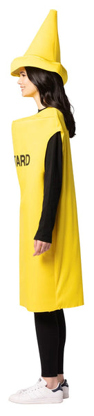 Side view of woman in Adults Mustard Bottle Costume Featuring a bright yellow bottle-shaped tunic with a smooth fabric finish and a wide, sleeveless cut that drapes over the body to mid-thigh length. The front displays bold black lettering spelling mustard, and the costume is paired with a matching oversized hat designed to resemble a pointed squeeze-bottle cap with a circular base brim. 