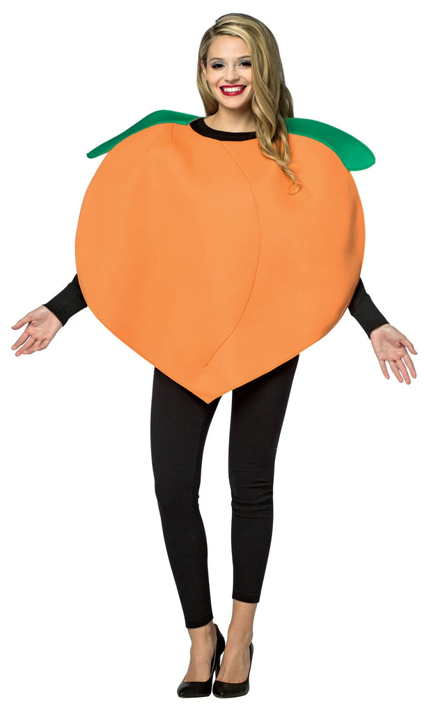 Woman posing in the Adults Pleasant Peach Costume Featuring a large orange poly-foam tunic shaped like a rounded peach with a smooth surface, subtle center seam detail, and two attached green leaf accents at the neckline, designed in a loose, wearable silhouette that slips on easily over clothing.