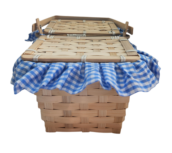 Boots and Brother's Puppy in a Basket featuring a woven natural wood basket with a handle, lined with a blue and white gingham fabric ruffle, closed, front view