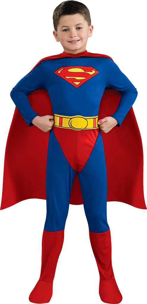 Boy posing in the DC Universe Classic Superman Costume featuring a full‑body long‑sleeve jumpsuit in bold blue with bright red lower accents, designed with a clean, streamlined silhouette that showcases Superman’s iconic look; the chest is printed with the unmistakable red‑and‑yellow “S” shield emblem, while a bright yellow printed belt adds contrast at the waist. The costume includes a flowing red cape, completing the classic superhero profile from head to toe