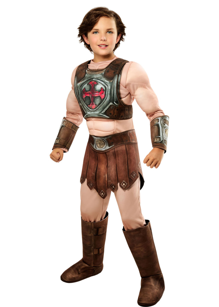 Boy posing in the Boys Deluxe Masters Of The Universe He-Man Costume Featuring a full costume set including a flesh-toned jumpsuit with built-in muscle padding on the chest, arms, and legs, a molded chest armor piece with metallic detailing and a red cross emblem at the center, a brown faux leather-style loincloth skirt with stitched panel accents, matching wrist gauntlets, a wide belt with buckle detail, and tall boot tops that complete the armored warrior look.