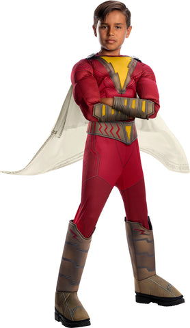 Boy posing in Deluxe Shazam Costume featuring a full‑body red superhero jumpsuit designed with a lightly padded muscle torso and arms to create a strong, heroic silhouette; the chest is prominently printed with Shazam’s iconic gold lightning bolt emblem set against a bright yellow burst panel for instant comic‑book recognition. Included is a wide printed belt with lightning‑inspired detailing, matching gold‑accented forearm cuffs, tall boot covers with molded lightning designs, and a flowing off‑white cape