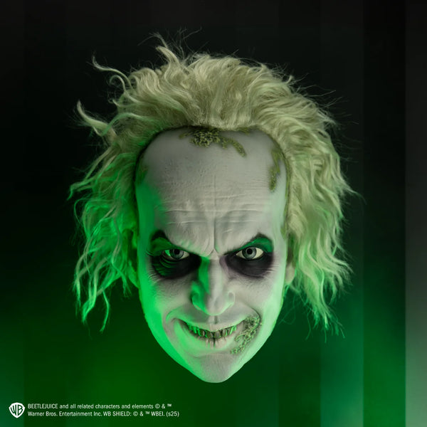 Deluxe Beetlejuice Injection Costume Mask features a gnarly yellow‑green complexion, pale, white cheeks and complexion, a wide crooked grin packed with uneven, decayed yellow teeth, eyes rimmed with dark purple bags and shading, heavy wrinkle lines across the brow and mouth, and moss like details along the side of the mouth and hairline with matching wild, frizzy green hair attached, cinematic image