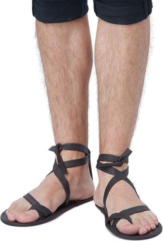 Man wearing the Egyptian Costume Sandals Featuring a pair of flat, black costume sandals designed with a simple sole and multiple thin straps across the toes and foot, connected to long attached laces that wrap around the ankle and lower leg for an adjustable and secure fit.