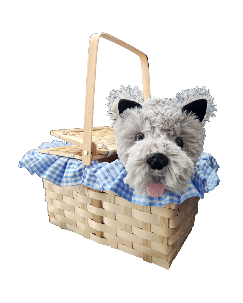 Front view of a woven picnic basket with a light wood handle, lined with blue and white gingham fabric, featuring a plush gray dog toy peeking out from inside 