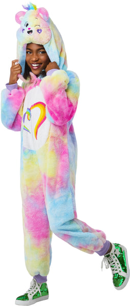 Girl posing Togetherness Bear Costume featuring soft, plush one‑piece jumpsuit covered in a pastel rainbow tie‑dye pattern blending pink, blue, yellow, and purple tones; a cozy hood shaped like the Togetherness Bear, complete with rounded bear ears, an embroidered smiling face, and small heart details on the cheeks. Front of the costume includes a white belly panel printed with the signature rainbow heart Care Bears symbol, while the back is finished with an attached fluffy pink bear tail and a small heart 