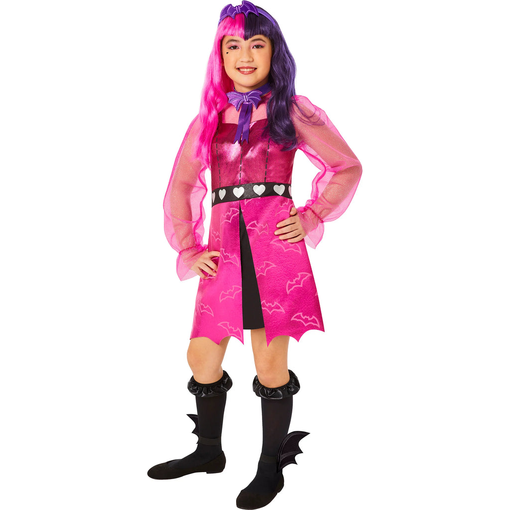Girl posing in the Girls Monster High Draculara Costume Featuring a pink dress with a metallic sheen and bat print pattern on the skirt, designed with a fitted bodice, sheer long sleeves, and a black waistband accented with heart details, paired with a bat-shaped bow tie, a matching headpiece with bat-inspired design, black knee-high socks, and ankle accessories shaped like bat wings.