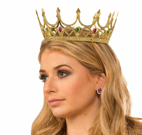  Woman modeling Gold Royal Queen Crown Costume Accessory featuring an elegant gold‑tone crown with a delicate openwork design, tall, pointed arches, and finely textured detailing throughout; accented with jewel‑tone faux gemstones in rich red and deep green set into the front, adding contrast and regal color; secured with an elastic strap
