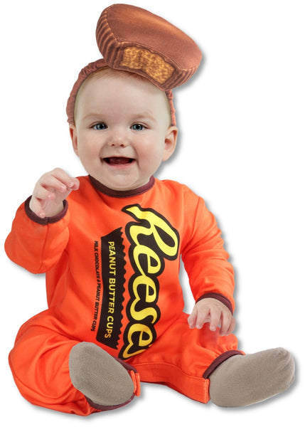 Baby wearing the Reese's Peanut Butter Cup costume featuring a bright orange one‑piece jumpsuit styled to look like a classic Reese’s package, printed with bold yellow and black “Reese’s” lettering across the front along with a vertical “Peanut Butter Cups” graphic panel; designed with long sleeves and brown trim accents at the cuffs. The look is completed with a soft plush Reese’s peanut butter cup headpiece, shaped like the iconic chocolate treat