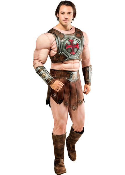 Man posing in the Mens Deluxe Masters Of The Universe He-Man Costume Featuring a full-body costume set including a flesh-toned jumpsuit with built-in muscle padding on the chest, arms, and legs, a molded chest armor piece with metallic detailing and a red cross emblem at the center, a brown faux leather-style loincloth skirt with stitched panel accents, coordinating arm bracers, a wide belt with buckle detail, and tall boot tops designed to create a cohesive armored warrior look.