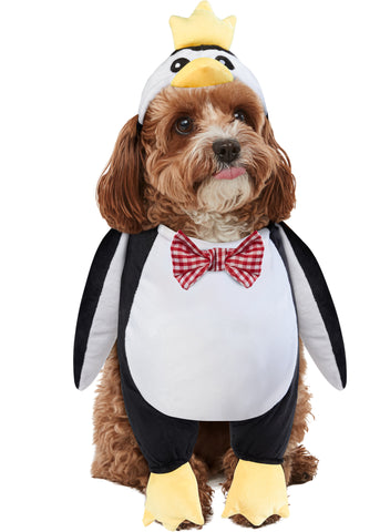Cockapoo puppy modeling the Pets Walking Penguin Costume which features a plush, full‑body penguin "walking" illusion in classic black‑and‑white coloring with a soft white belly panel, black flipper‑style sides, and oversized yellow plush feet and an attached penguin character hood with embroidered eyes, a soft yellow beak, and a bright yellow crown perched on top, along with a red‑and‑white checkered bow tie
