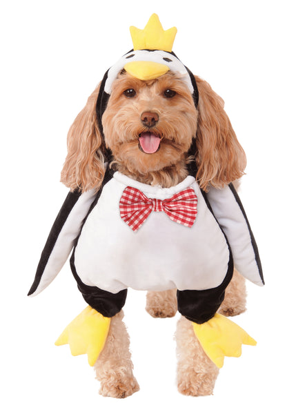 Poodle modeling the Pets Walking Penguin Costume which features a plush, full‑body penguin "walking" illusion in classic black‑and‑white coloring with a soft white belly panel, black flipper‑style sides, and oversized yellow plush feet and an attached penguin character hood with embroidered eyes, a soft yellow beak, and a bright yellow crown perched on top, along with a red‑and‑white checkered bow tie