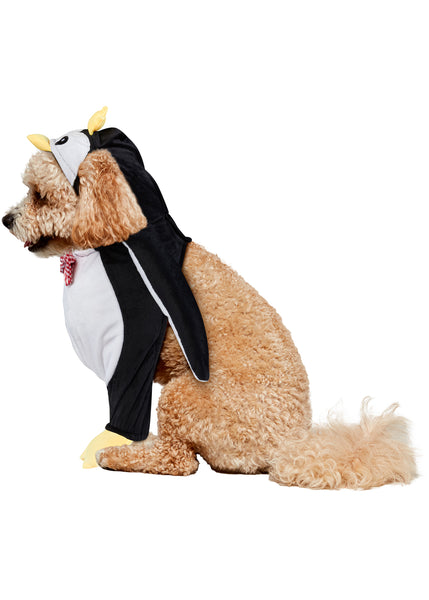 Poodle side view of Pets Walking Penguin Costume which features a plush, full‑body penguin "walking" illusion in classic black‑and‑white coloring with a soft white belly panel, black flipper‑style sides, and oversized yellow plush feet and an attached penguin character hood with embroidered eyes, a soft yellow beak, and a bright yellow crown perched on top, along with a red‑and‑white checkered bow tie