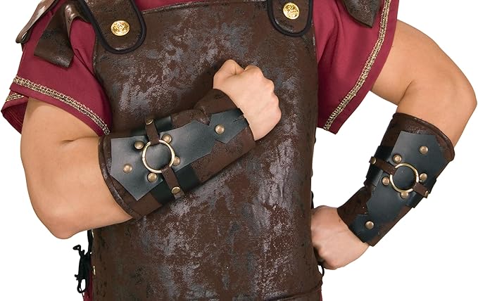 Man posing in the Roman Soldier Arm Guards which feature a matching pair of wide forearm guards crafted in layered faux‑leather materials, designed in deep brown and dark charcoal tones for a rugged, battle‑ready appearance; each guard is detailed with gold‑tone round studs, circular ring accents at the center, and reinforced paneling that wraps fully around the forearm, creating a strong, armored silhouette inspired by ancient Roman soldier gear