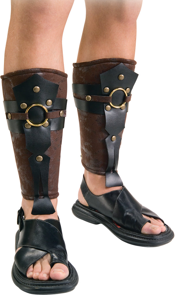 Featuring a matching pair of shin‑high armored leg coverings designed in textured brown faux‑leather, shaped to wrap securely around the lower legs from calf to ankle. Each guard is accented with layered black faux‑leather straps, round gold‑tone studs, and a prominent circular gold ring centerpiece at the front, creating a structured, battle‑ready look inspired by ancient Roman armor. The guards taper cleanly at the ankle with strap extensions that sit just above the foot
