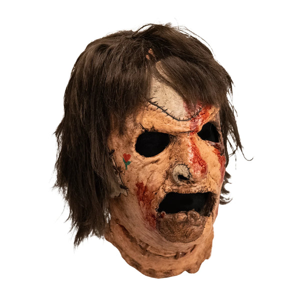 The Texas Chainsaw Massacre 3 III Leatherface Costume Mask of a latex full-head Leatherface mask with grimacing expression, stitched skin details, bloody patches, little rose heart tattoo on the cheek, and attached hair, right side profile