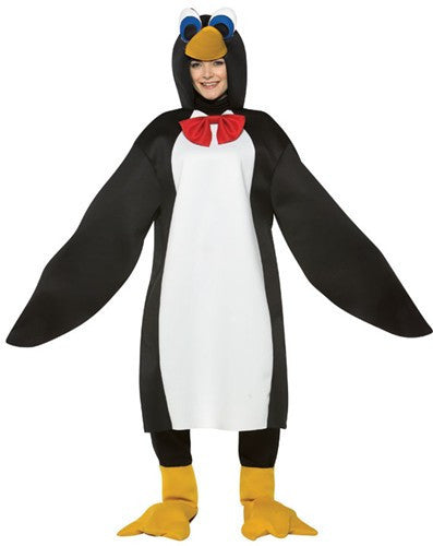 Woman in the Adults Penguin Costume Featuring a black and white penguin tunic with a smooth fabric finish, designed with a white front panel and attached elongated wing-style sleeves. The costume includes an attached hood with a sculpted penguin beak and large cartoon-style eyes, along with a red bow tie at the neckline. Matching yellow penguin feet shoe covers slip over footwear, completing the look with webbed detailing and a soft, rounded shape.